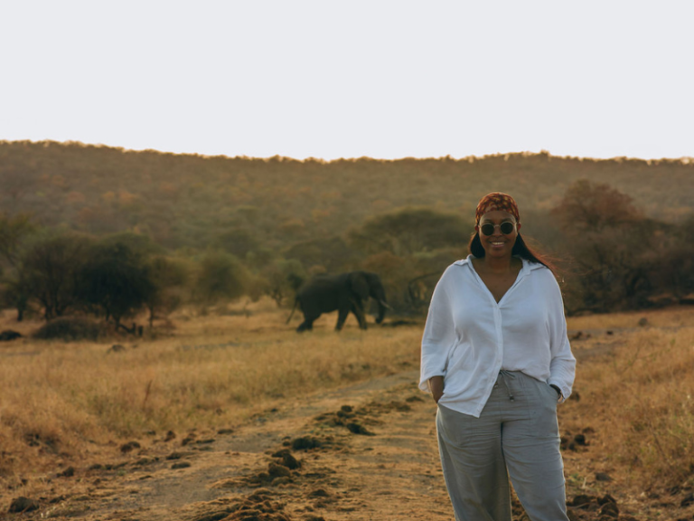 Traveler walking along a dirt track with an elephant in the background, a memorable moment often experienced on africa group tours.