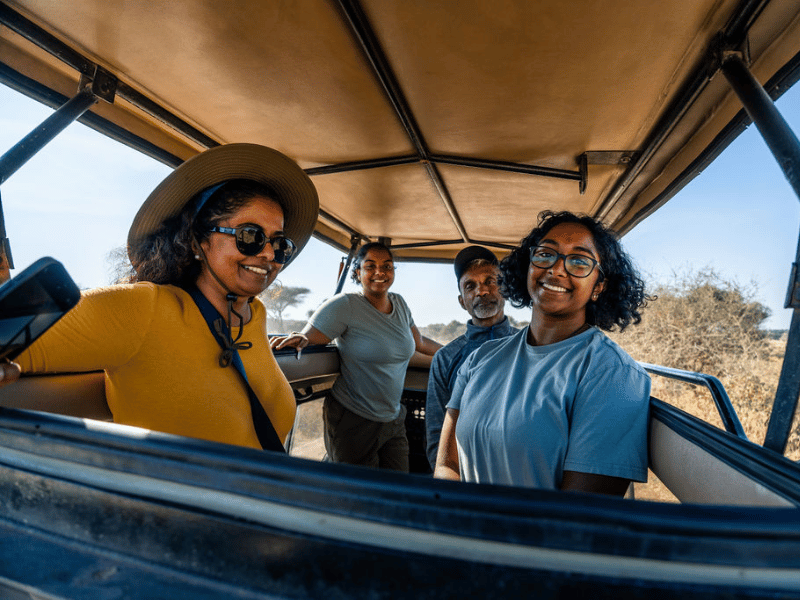 Custom African Safaris: What Bespoke Really Means 1 A smiling group of travelers enjoying their Tanzania safari inside an open-roof safari vehicle, with golden savanna in the background.