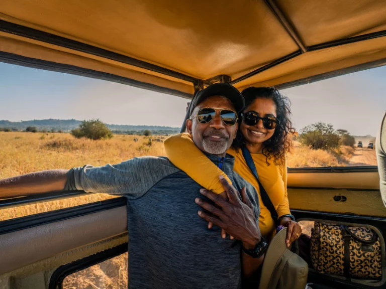 Happy couple sitting together inside an open safari vehicle, framed by golden grasslands and warm sunlight.