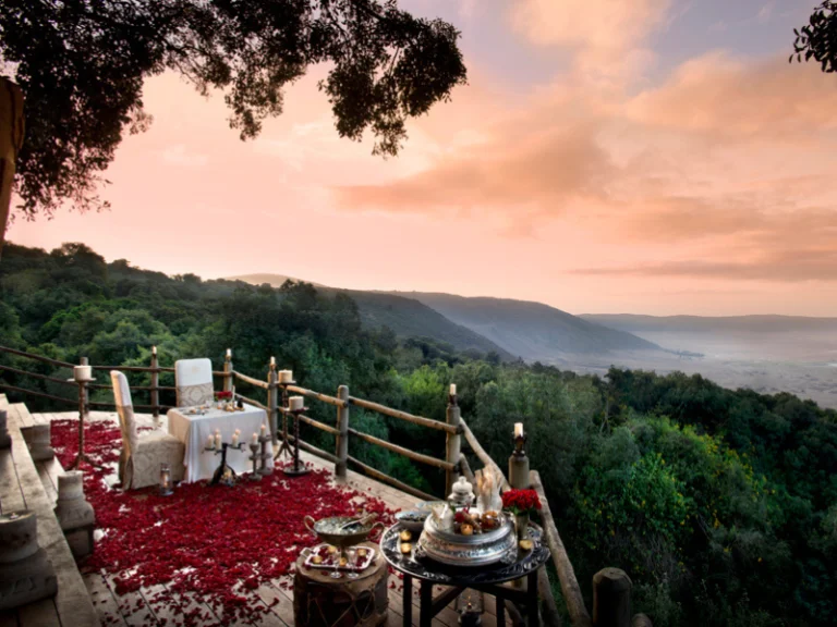 Candlelit private dinner setup on a deck overlooking a lush valley at sunset, creating the perfect atmosphere for romantic african safaris.