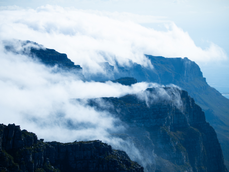 Dramatic clouds sweeping over the rugged peaks of Table Mountain in South Africa, creating a surreal, misty landscape.