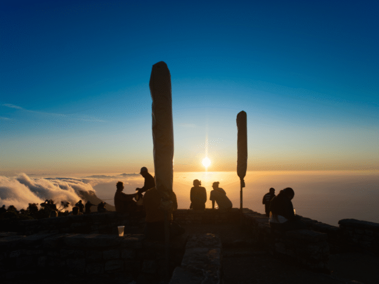 Silhouetted visitors enjoying a stunning sunset above the clouds from a scenic viewpoint on top of Table Mountain.