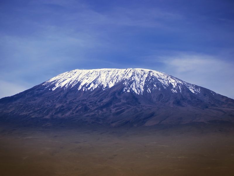 Snow-capped Mount Kilimanjaro rising above the plains of Tanzania under a clear blue sky, a breathtaking view often used to describe mt kilimanjaro hike difficulty.