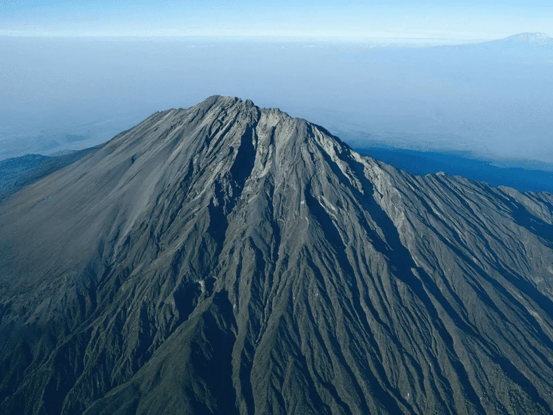 Aerial view of Mt Meru's rugged summit with deep ridges and steep volcanic slopes, showcasing the raw beauty of the Tanzanian highlands.