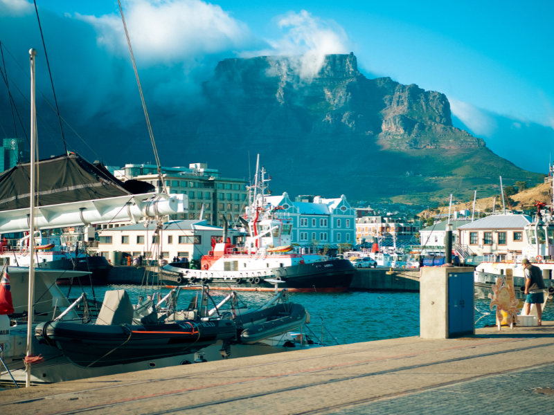 Colorful boats docked at the V&A Waterfront in Cape Town with Table Mountain rising majestically in the background on a cloudy day.