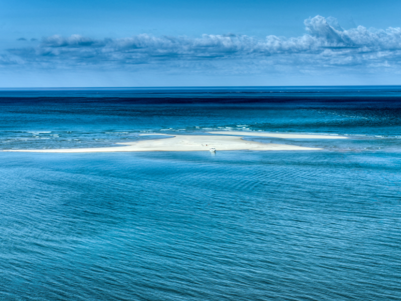 Crystal-clear turquoise waters surrounding a small white sand island off Mozambique’s coast under a bright blue sky
