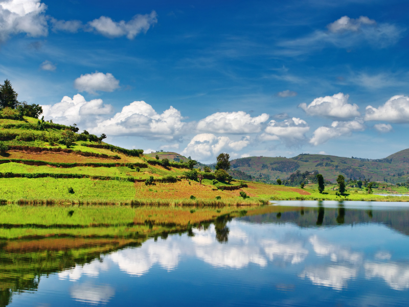 Terraced green hills reflecting perfectly in the calm blue waters of a highland lake, one of the scenic places to visit in Uganda.