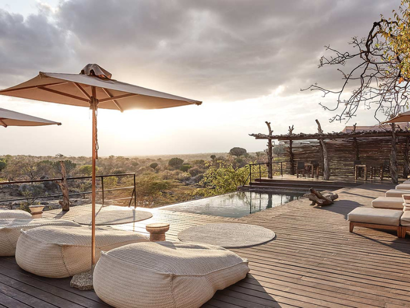 What’s Included in Luxury Tanzania Safaris (and Why They’re Worth It) 2 Sunset view from a wooden safari deck with cushioned loungers, umbrellas and a small infinity pool overlooking a vast savannah landscape