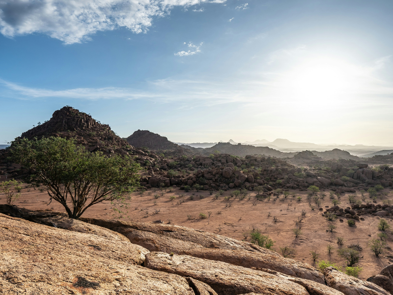 Sunlight over the rocky hills and dry terrain of Damaraland, Namibia, showcasing dramatic desert landscapes and scattered vegetation.