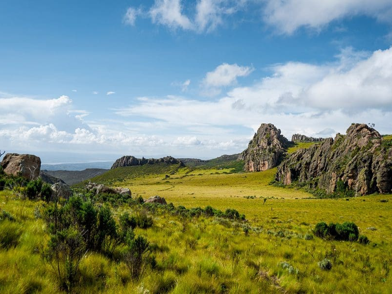 Wide grassy moorland and rocky outcrops under blue sky in Aberdare National Park.