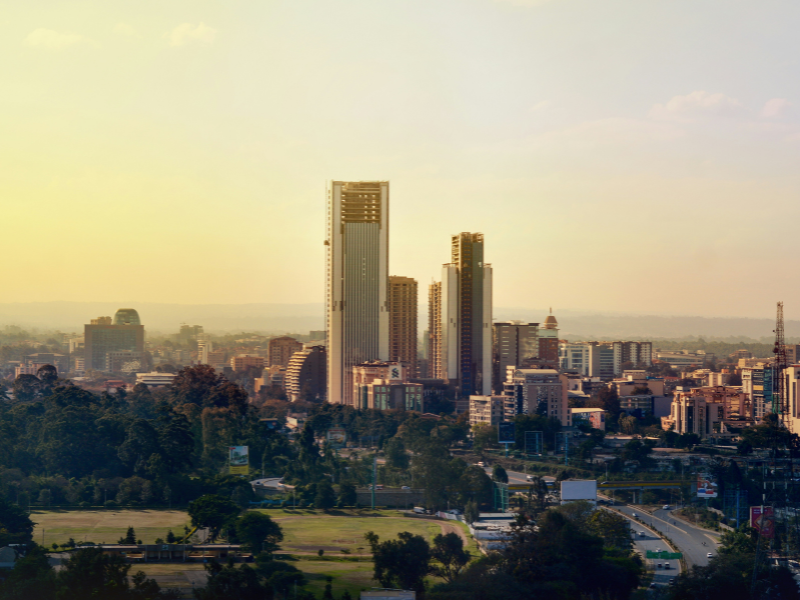 Skyline of Nairobi at sunset with tall buildings and green urban parks below.