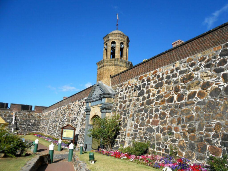 Stone walls and tower of the Castle of Good Hope under a bright blue sky.