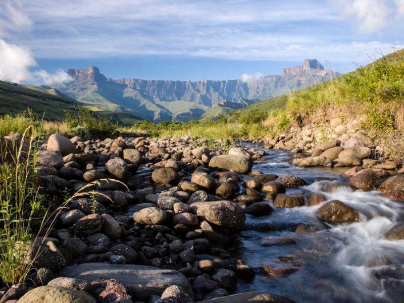 Rocky stream flowing through a green valley with dramatic mountain cliffs in the Drakensberg.