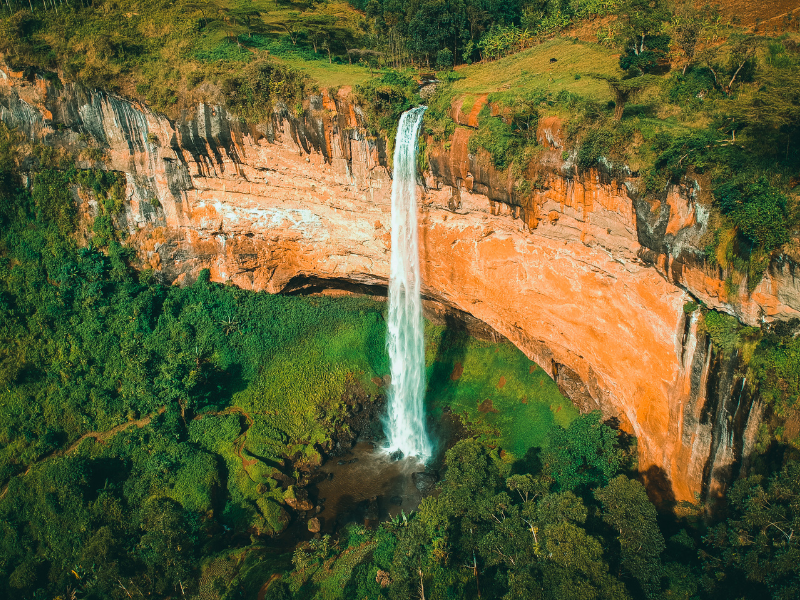 A tall waterfall plunging over a red cliff into lush greenery near Mount Elgon.