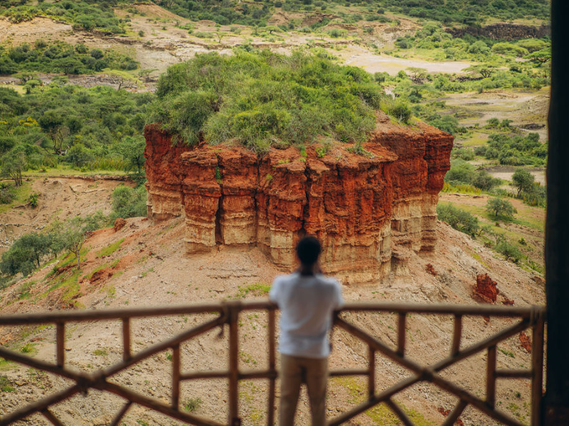 Man looking out at the landscape of Olduvai Gorge in Tanzania with layered red rock formations.