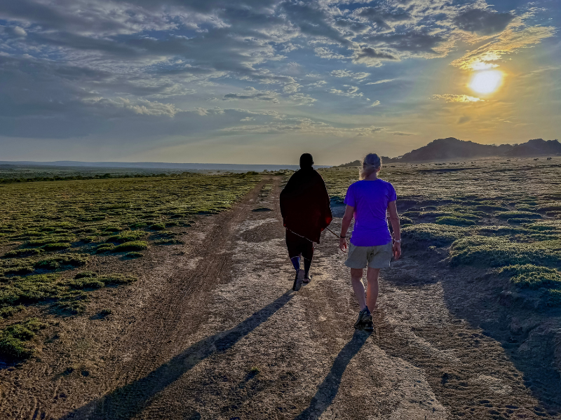 Traveler walking with a local guide at sunset on a dirt track, soaking in quiet landscapes and calm skies