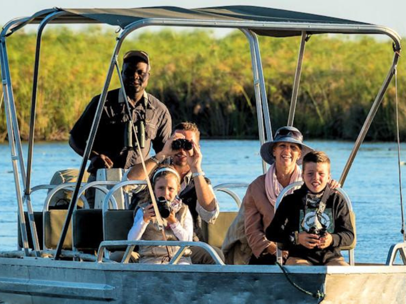 Family on a boat safari with a guide, spotting wildlife on family safaris in africa