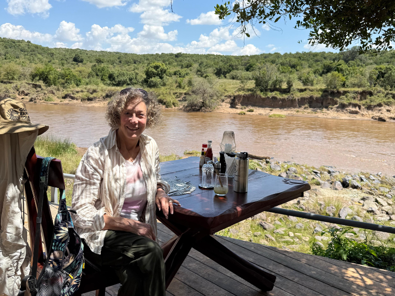 Traveler enjoying a relaxed riverside lunch with safari drinks overlooking a wide African river.