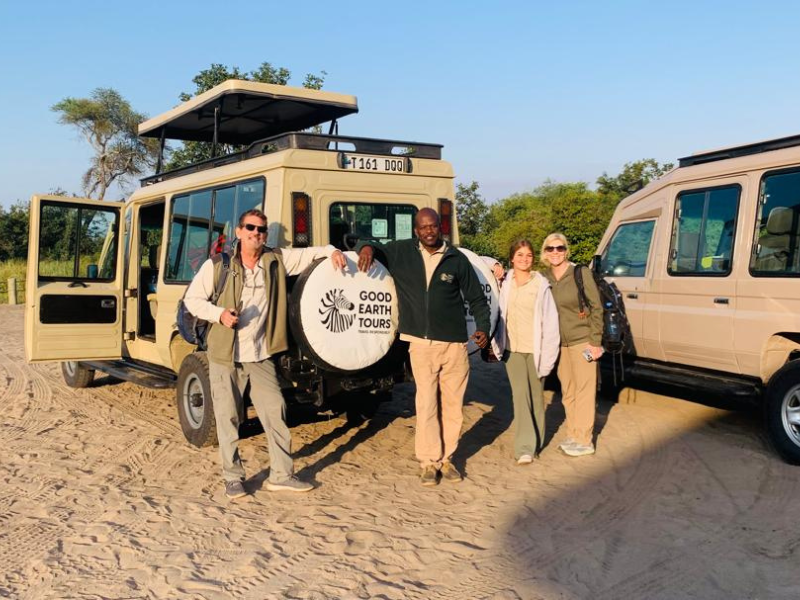 Good Earth Tours guests and guide posing beside safari vehicles before a game drive in Tanzania.