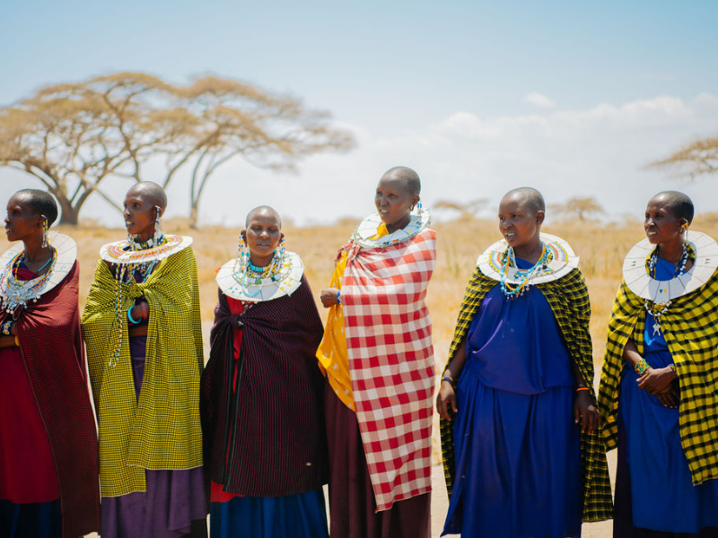 Maasai women standing together in colorful shukas and beaded jewelry on the savanna, sharing culture and community
