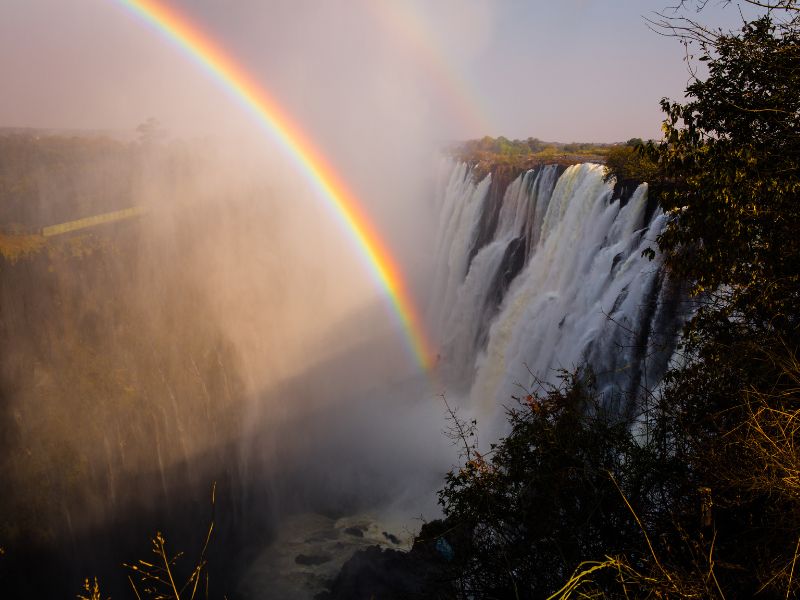 Victoria Falls in Zambia with rainbow mist rising above the waterfall.