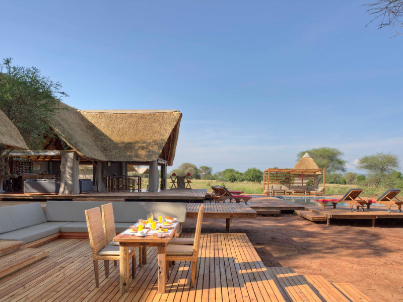 Open-air safari lodge with wooden deck, dining setup, and lounge chairs overlooking the African bush, offering a calm and comfortable place to relax between game drives.
