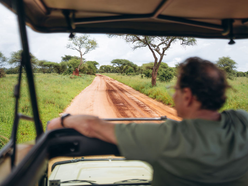 View from inside a safari vehicle driving along a dirt road through acacia-dotted landscape, capturing the rhythm of a game drive.