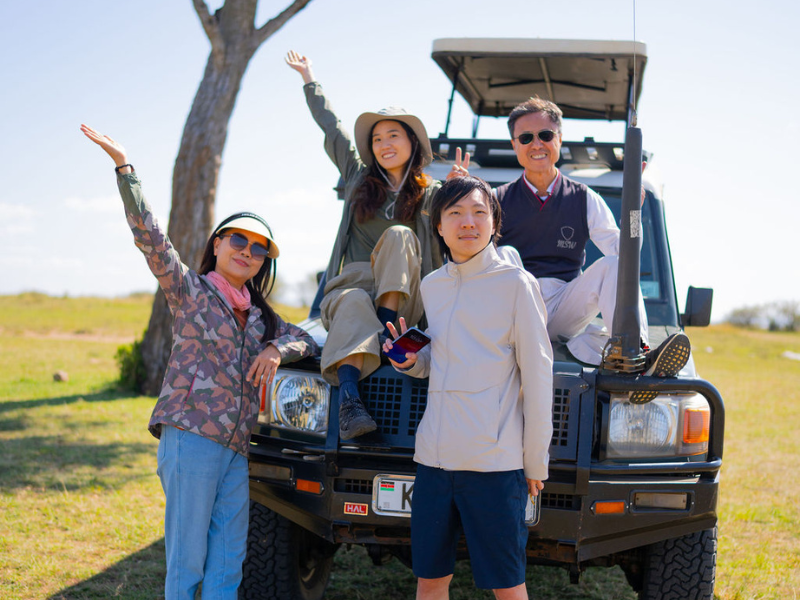 Friends posing on a safari vehicle in open grassland, smiling and celebrating their shared travel experience.