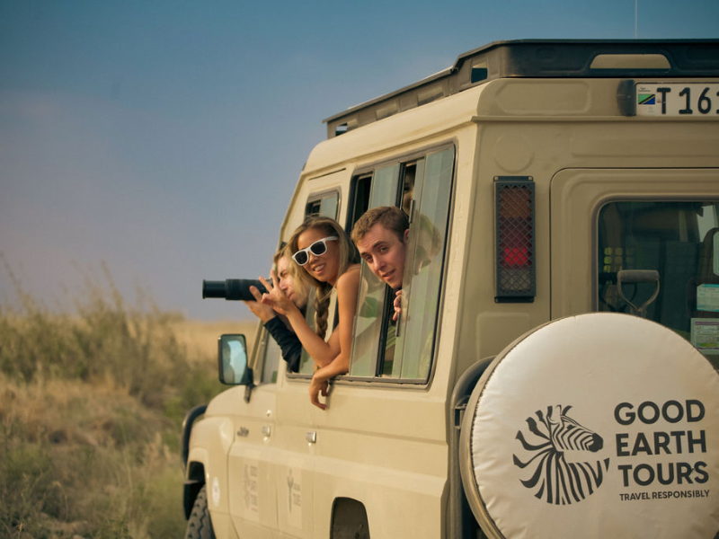 Traveler leaning out of an open safari vehicle watching elephants walk through golden grassland at close range, capturing a classic game drive moment.