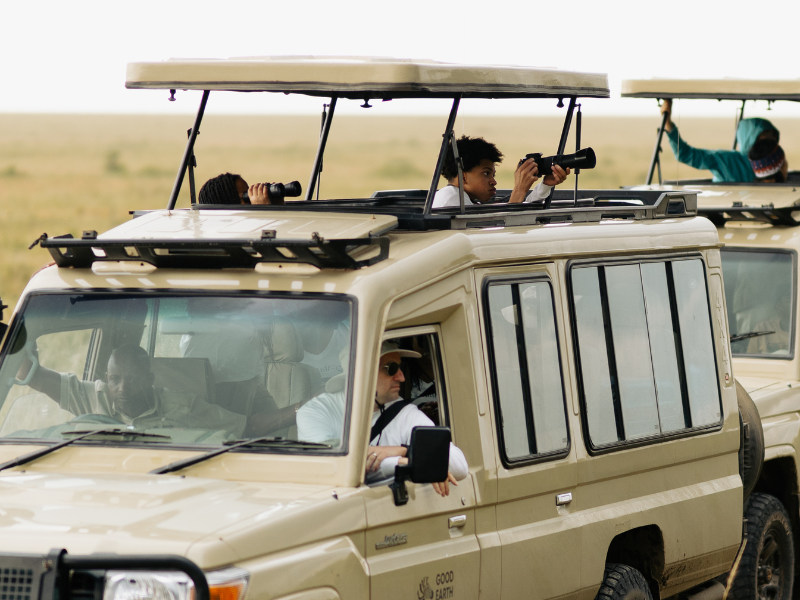 Travelers standing through the pop-up roof of a safari vehicle using cameras to photograph wildlife during a guided game drive.