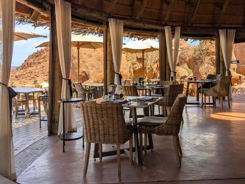 Best Places to Visit in Namibia: A First-Hand Guide 5 Open-air restaurant at Mowani Mountain Camp with wicker chairs and white drapes, red rock formations rising in the background, Damaraland Namibia