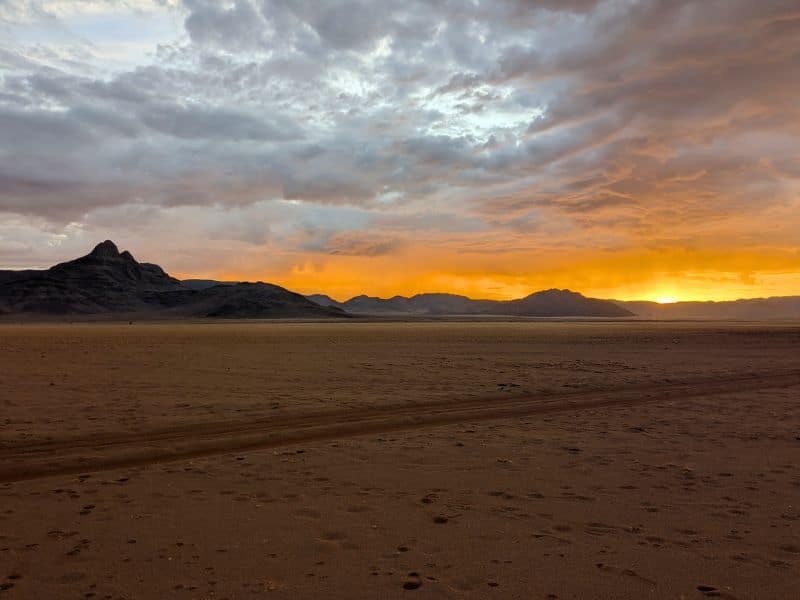 Best Places to Visit in Namibia: A First-Hand Guide 1 Fiery orange sunset over a vast desert plain with a lone mountain silhouette, NamibRand Nature Reserve Namibia